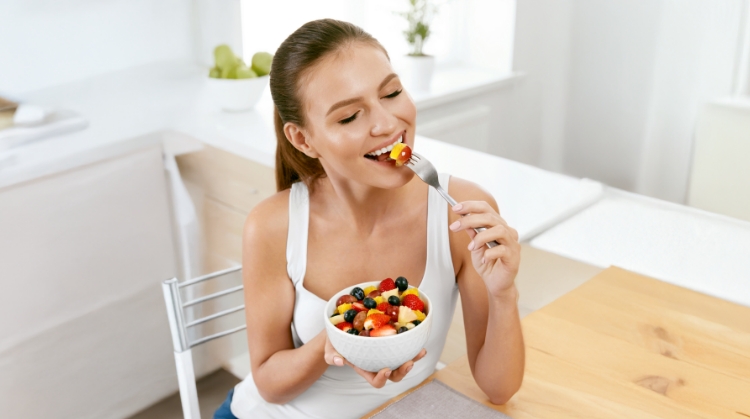 Smiling woman enjoying a fresh fruit salad, highlighting healthy eating tips for maintaining oral health during the holidays in Salt Lake City, UT.